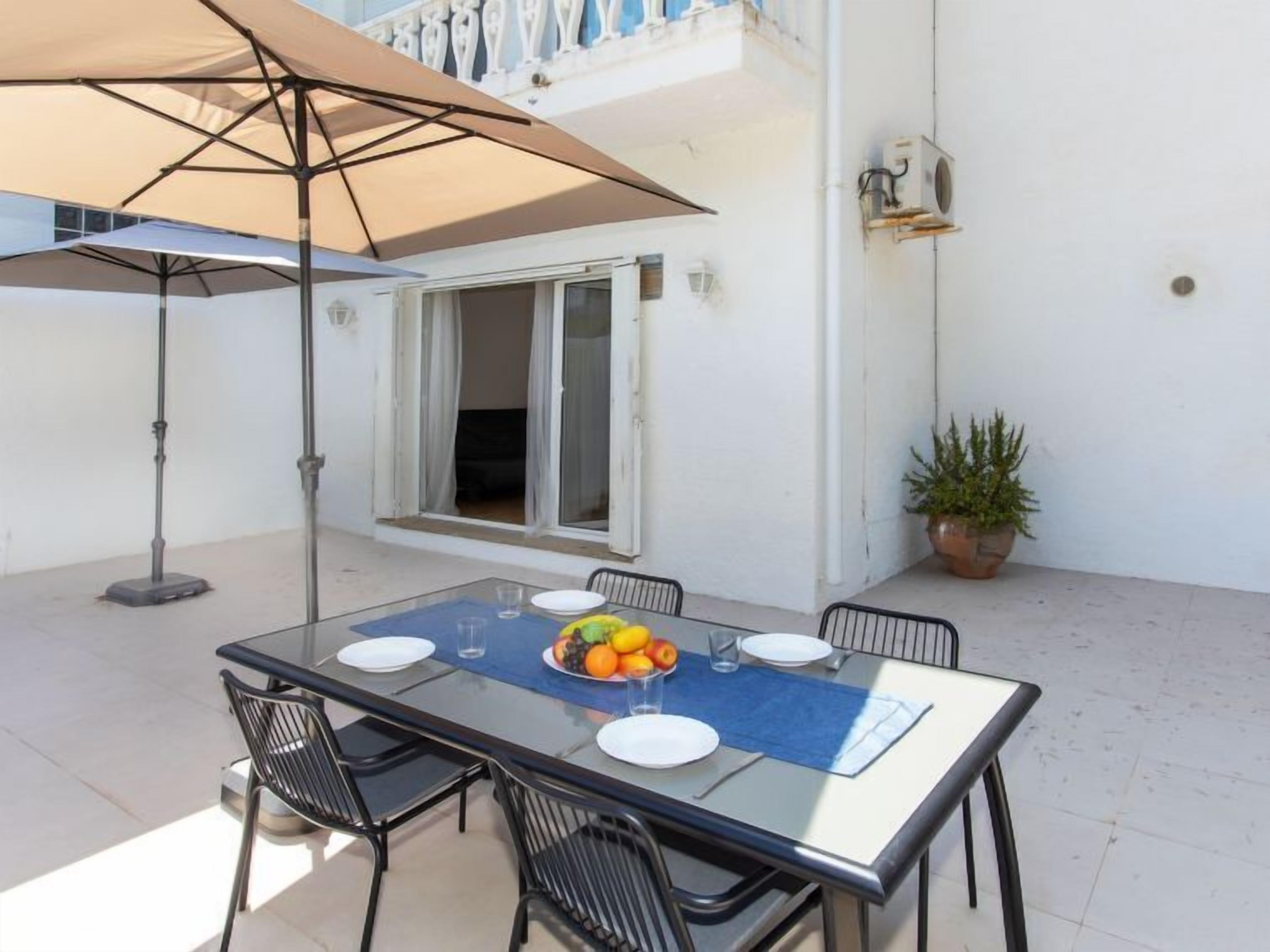 Een glazen tafel met vier stoelen, een schaal met fruit en een grote parasol.