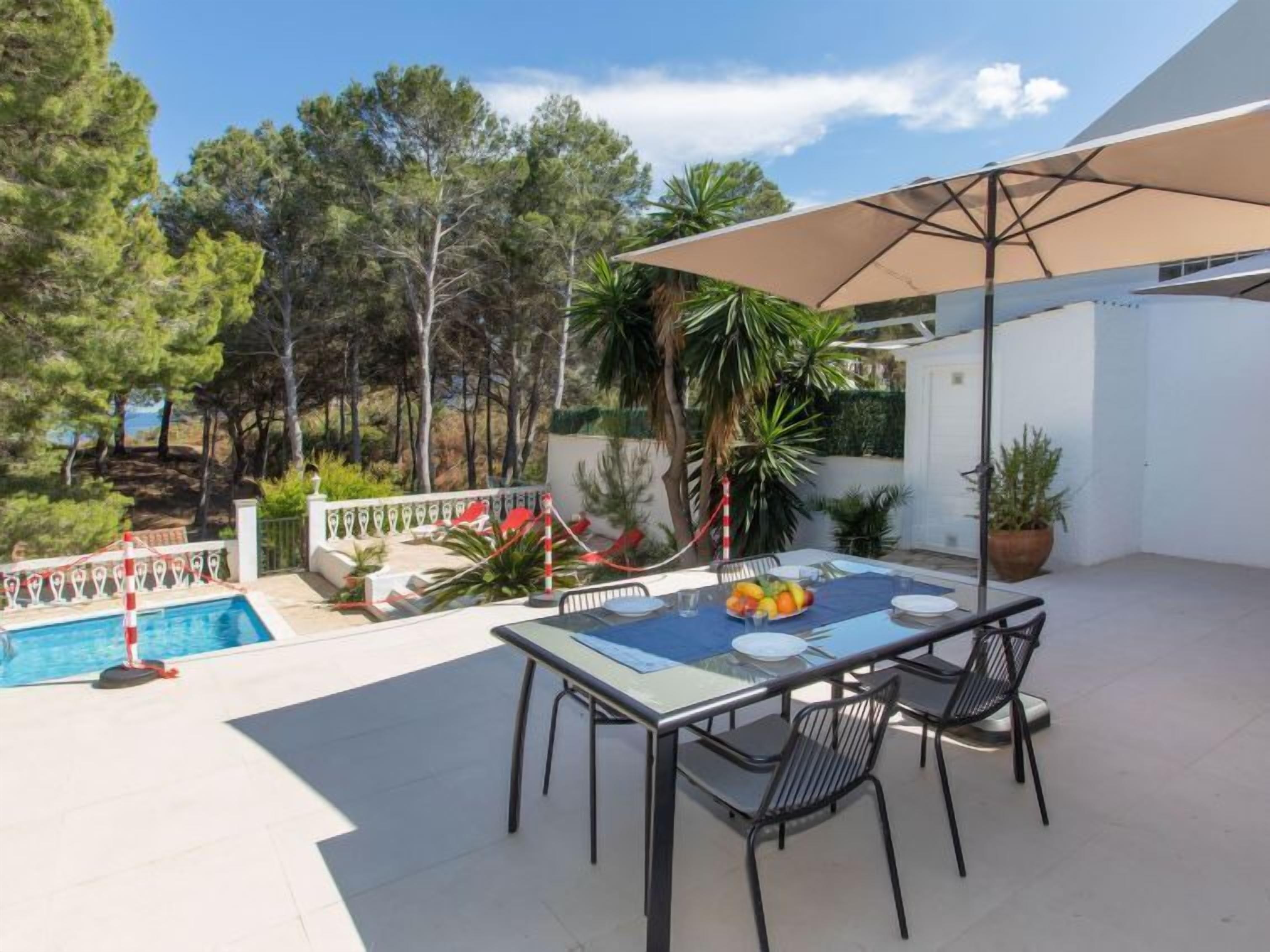 An outdoor patio with a table and chairs, a pool, and a view of trees and a building.