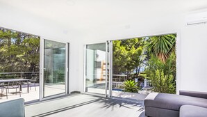 Una sala de estar moderna con un gran ventanal corredera que da a un balcón, amueblada con un sofá y una mesa de comedor.