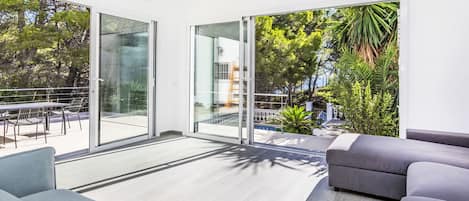 Una sala de estar moderna con un gran ventanal corredera que da a un balcón, amueblada con un sofá y una mesa de comedor.