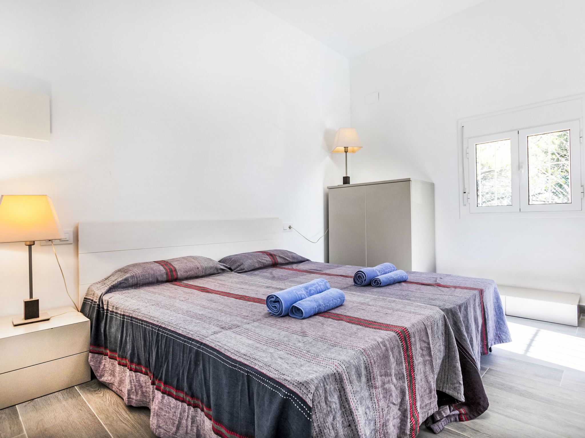 A bedroom with a bed, a nightstand, a lamp, a wardrobe, and a window.