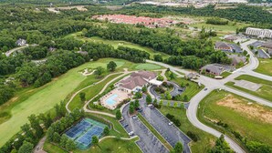 Vista aérea de un campo de golf con canchas de tenis, zonas de estacionamiento y edificios residenciales.