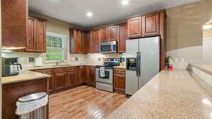 Una cocina con armarios de madera, electrodomésticos de acero inoxidable, encimeras de granito y un bote de basura.