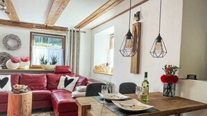 Spiseområde med et træbord dækket til fire personer, sofa i rødt læder med hjerteformede puder, og hængende geometriske pendellamper.