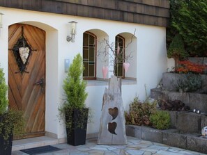 A building entrance with a wooden door, a stone sculpture with heart cutouts, and a potted plant. - Ehinger by Interhome (Eisenbach)
