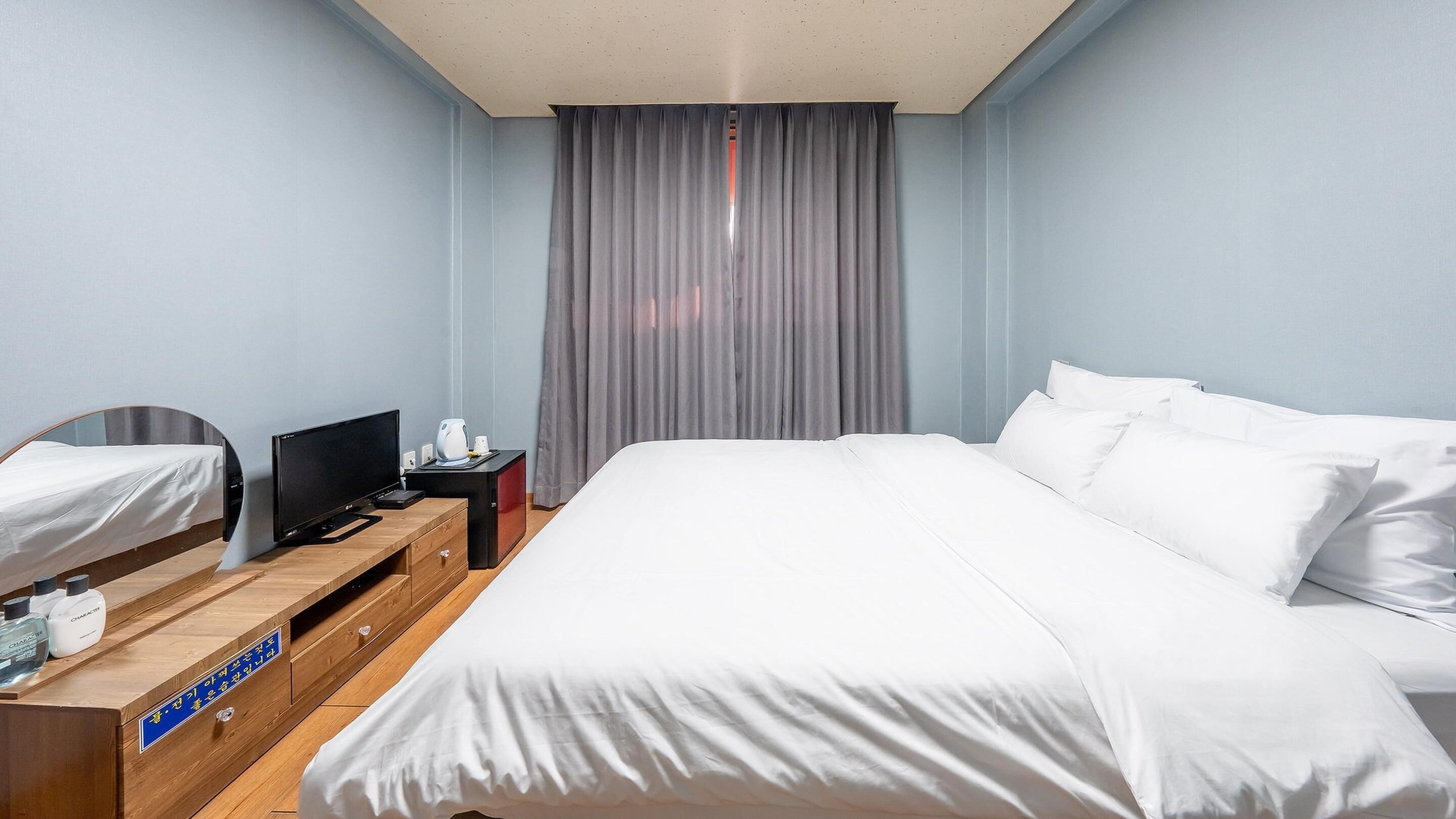 Een hotelkamer met een groot bed, een televisie op een houten dressoir en een raam met gordijnen.