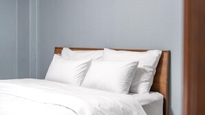 A neatly made bed with white linens and pillows, a wooden headboard, and a light blue wall. - Gyeongju Jang (Gyeongju)
