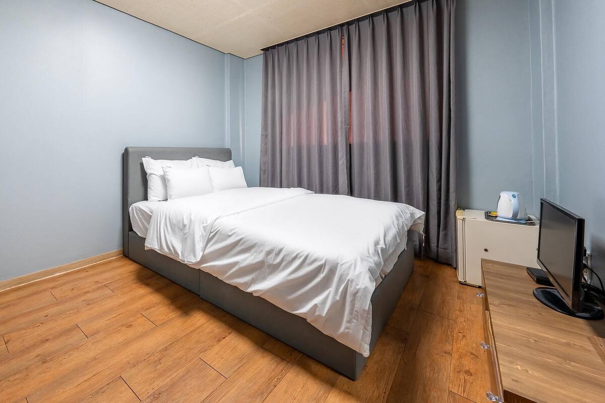A modern hotel room with a large bed, wooden flooring, a flat-screen TV, and a bedside table.