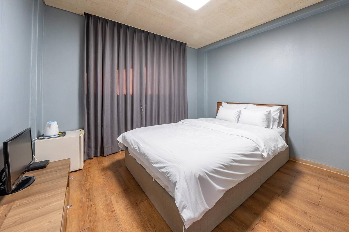A neatly made bed in a room with light blue walls and wooden flooring.