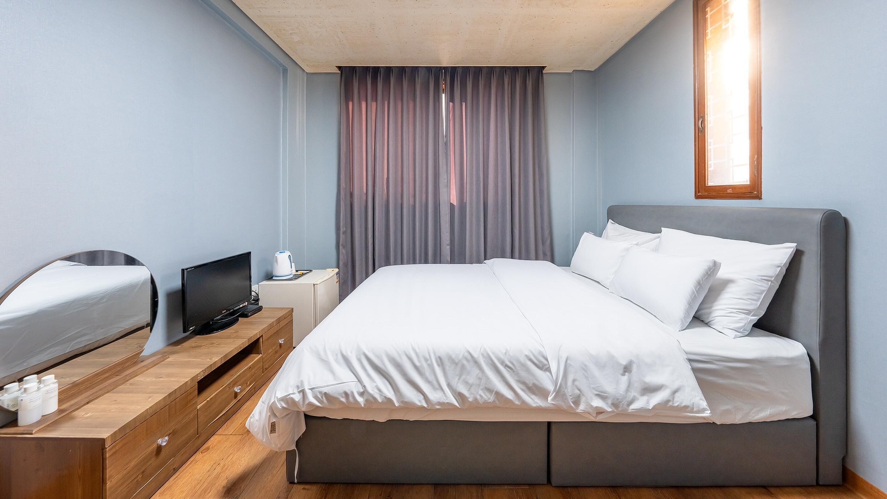 A hotel room with a bed, a desk with a computer, a TV, and a window with curtains.