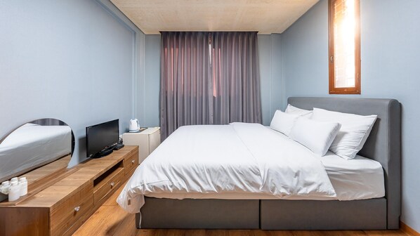A hotel room with a bed, a desk with a computer, a TV, and a window with curtains.