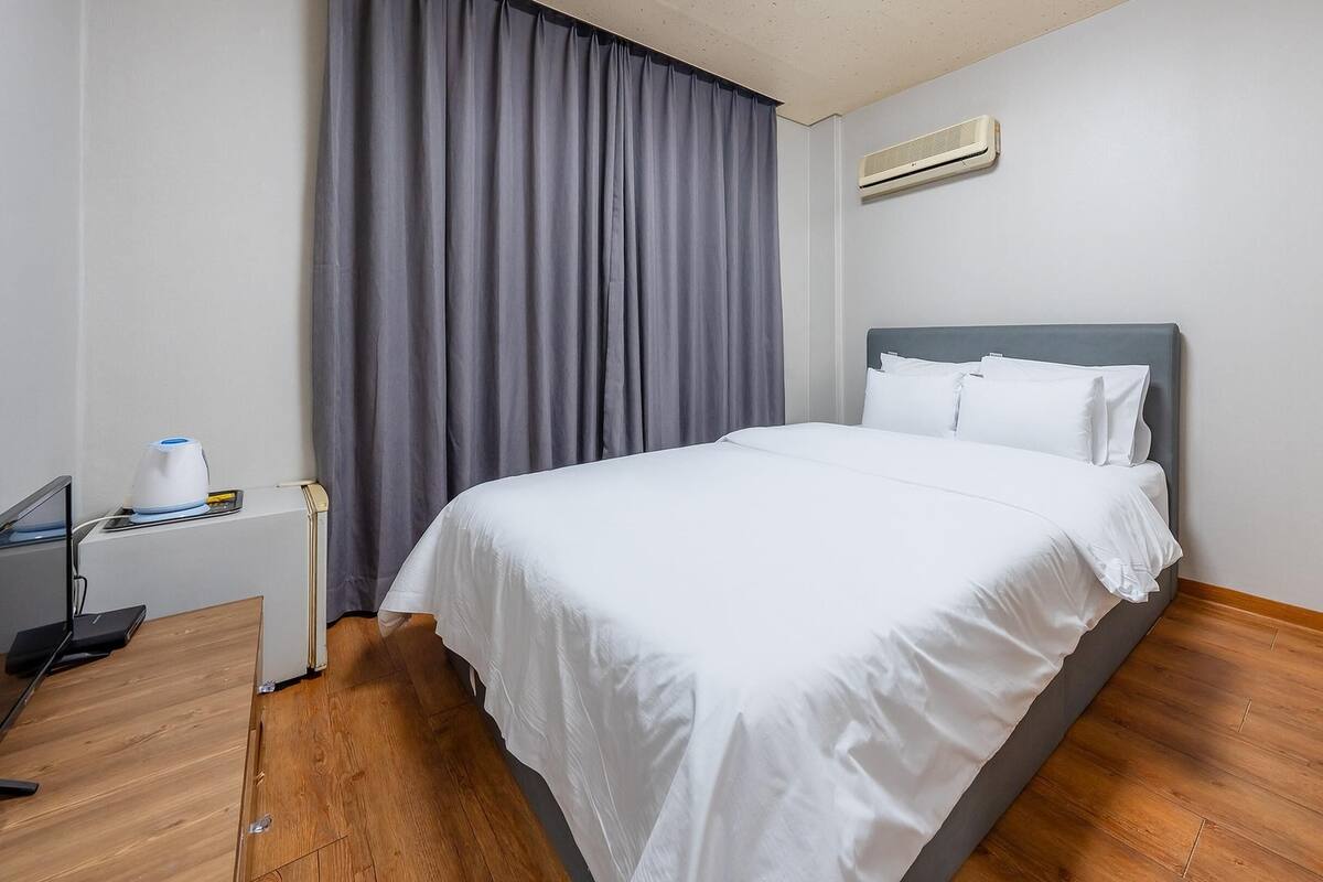 A hotel room with a bed, a desk, a chair, a coffee maker, and a window with curtains.