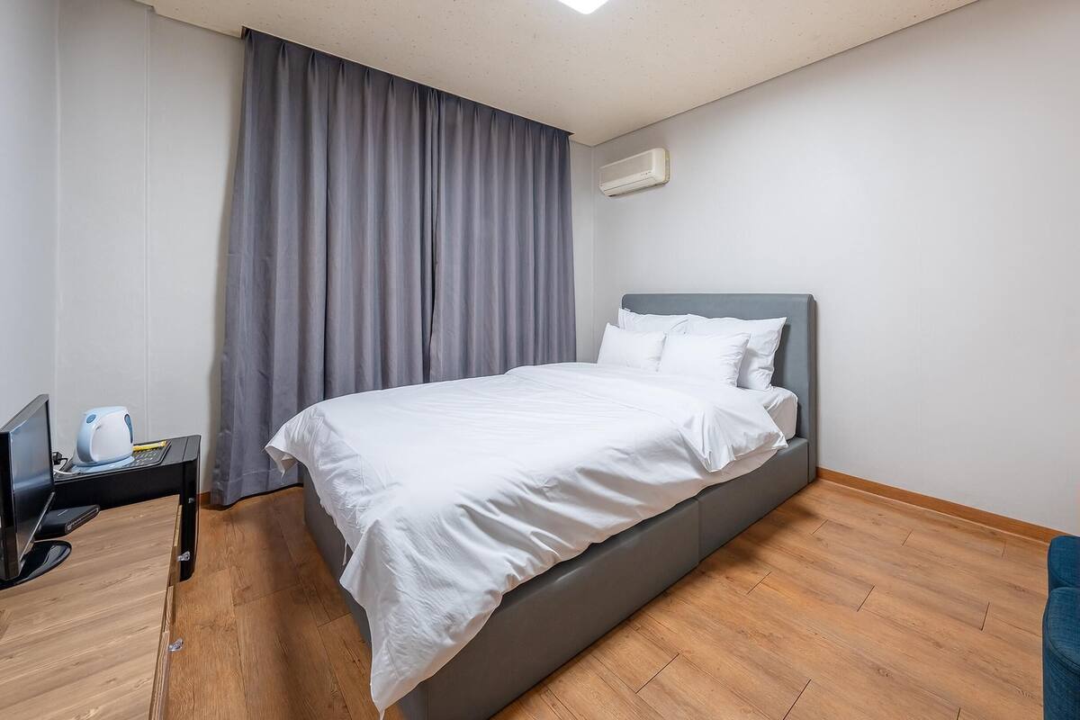 A hotel room with a bed, a desk with a laptop, a coffee maker, and a small table with a chair.
