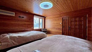 Una habitación con paredes y techo de madera, dos camas con ropa blanca, una ventana y una puerta.