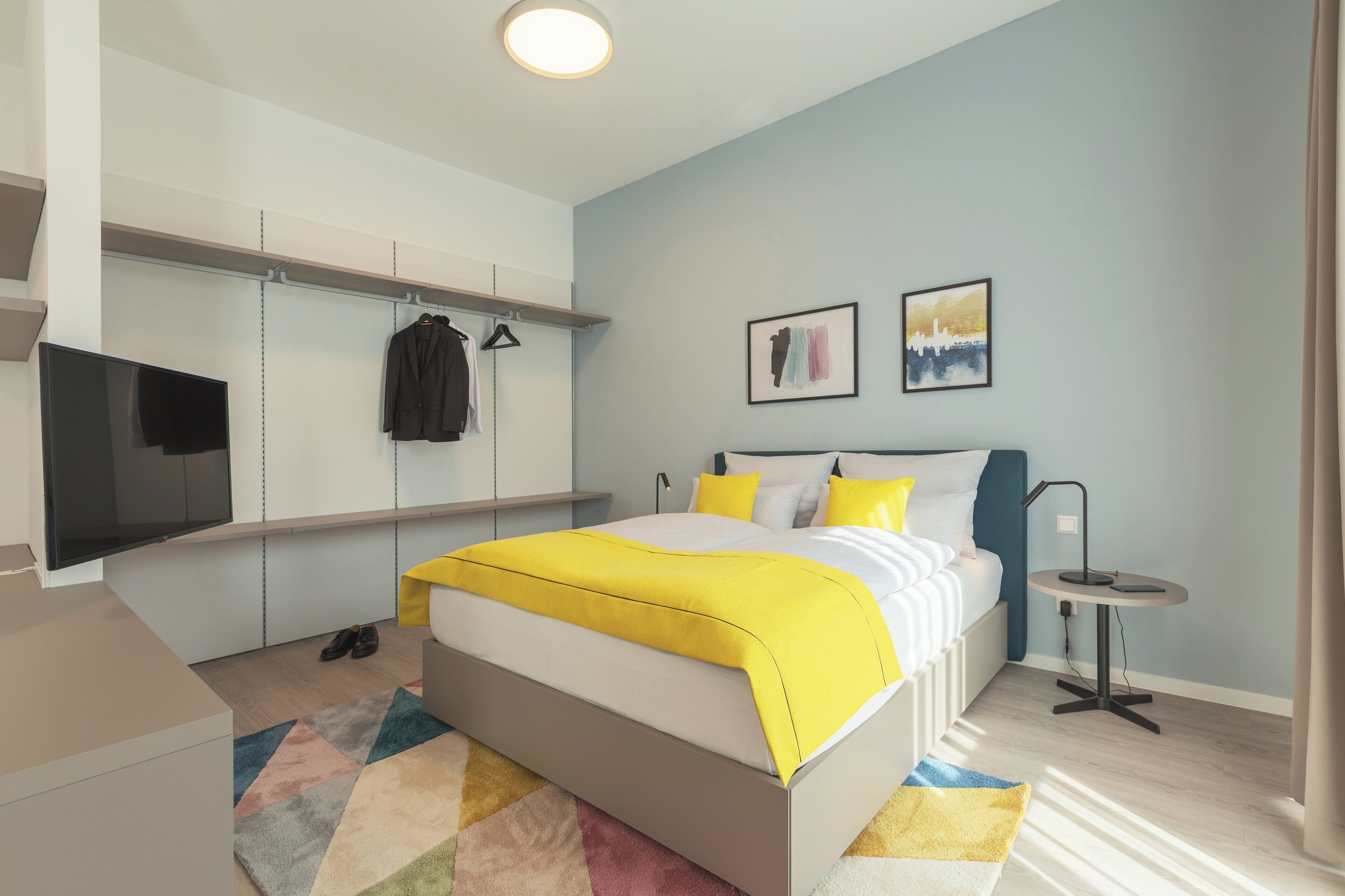 Ein modernes Schlafzimmer mit Bett, Fernseher, Kleiderschrank und einem kleinen Tisch.