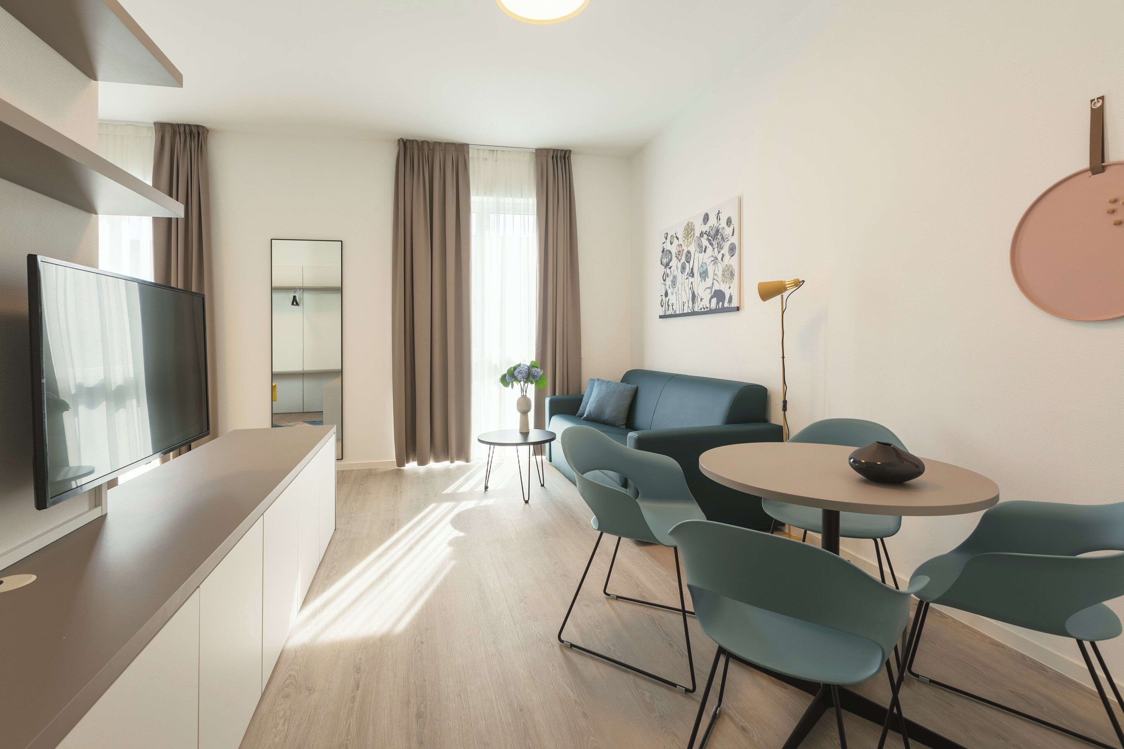 Un salon moderne avec un téléviseur à écran plat, un canapé, une table ronde et une petite table d’appoint sur laquelle est posée une plante.