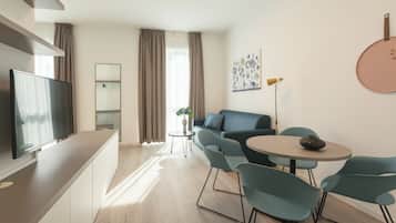 A modern living room with a flat-screen TV, a sofa, a round table, and a small side table with a plant.