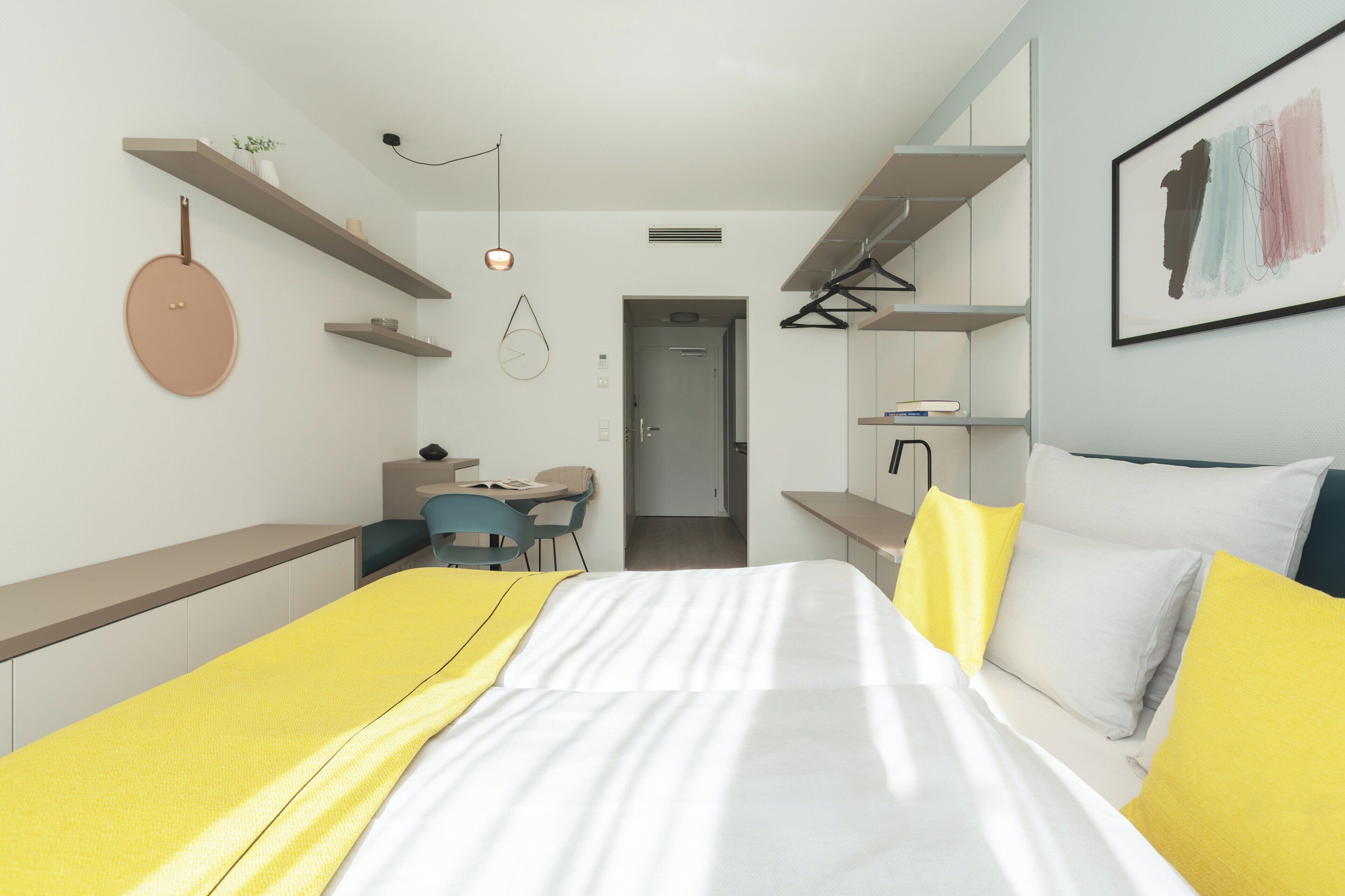 Un dormitorio moderno con cama, mesitas de noche, escritorio y silla. Hay una puerta que da a otra habitación.