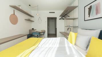 Un dormitorio moderno con cama, mesitas de noche, escritorio y silla. Hay una puerta que da a otra habitación.