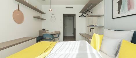 Un dormitorio moderno con cama, mesitas de noche, escritorio y silla. Hay una puerta que da a otra habitación.