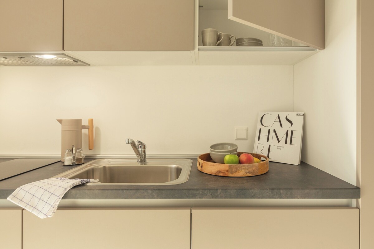 Una cocina moderna con un lavamanos de acero inoxidable, un cuenco de madera con frutas y una revista sobre la encimera.