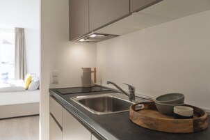 A modern kitchen with a stainless steel sink, a wooden tray with bowls, and a window with curtains.