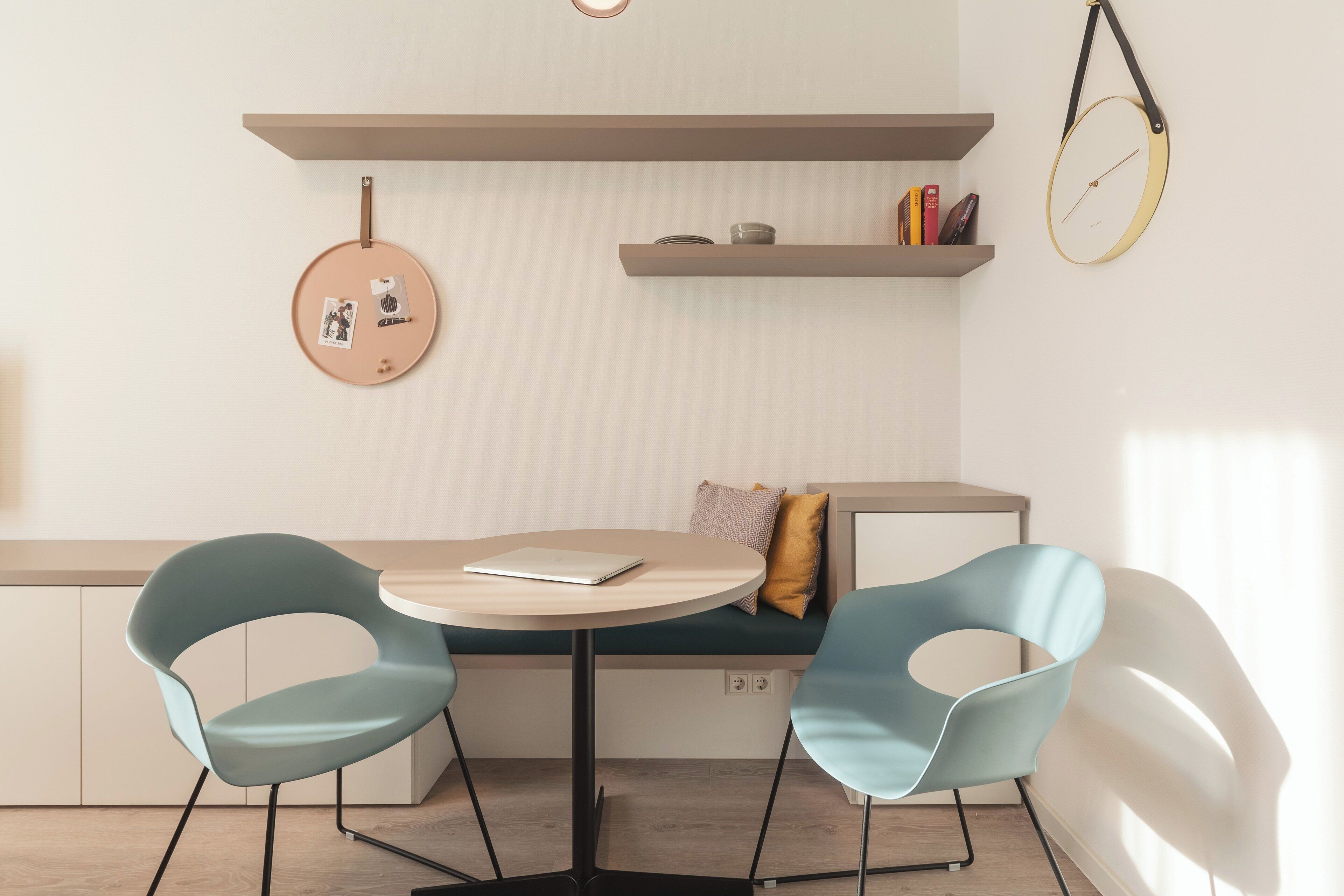 Una habitación moderna con una mesa redonda, dos sillas, un banco y un reloj en la pared.