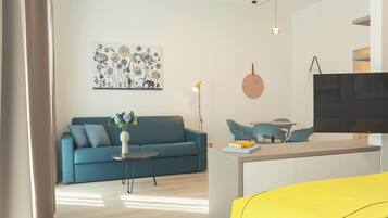 A modern living room with a blue sofa, a small round table, and a coffee table. There is a painting on the wall and a TV mounted on the wall.