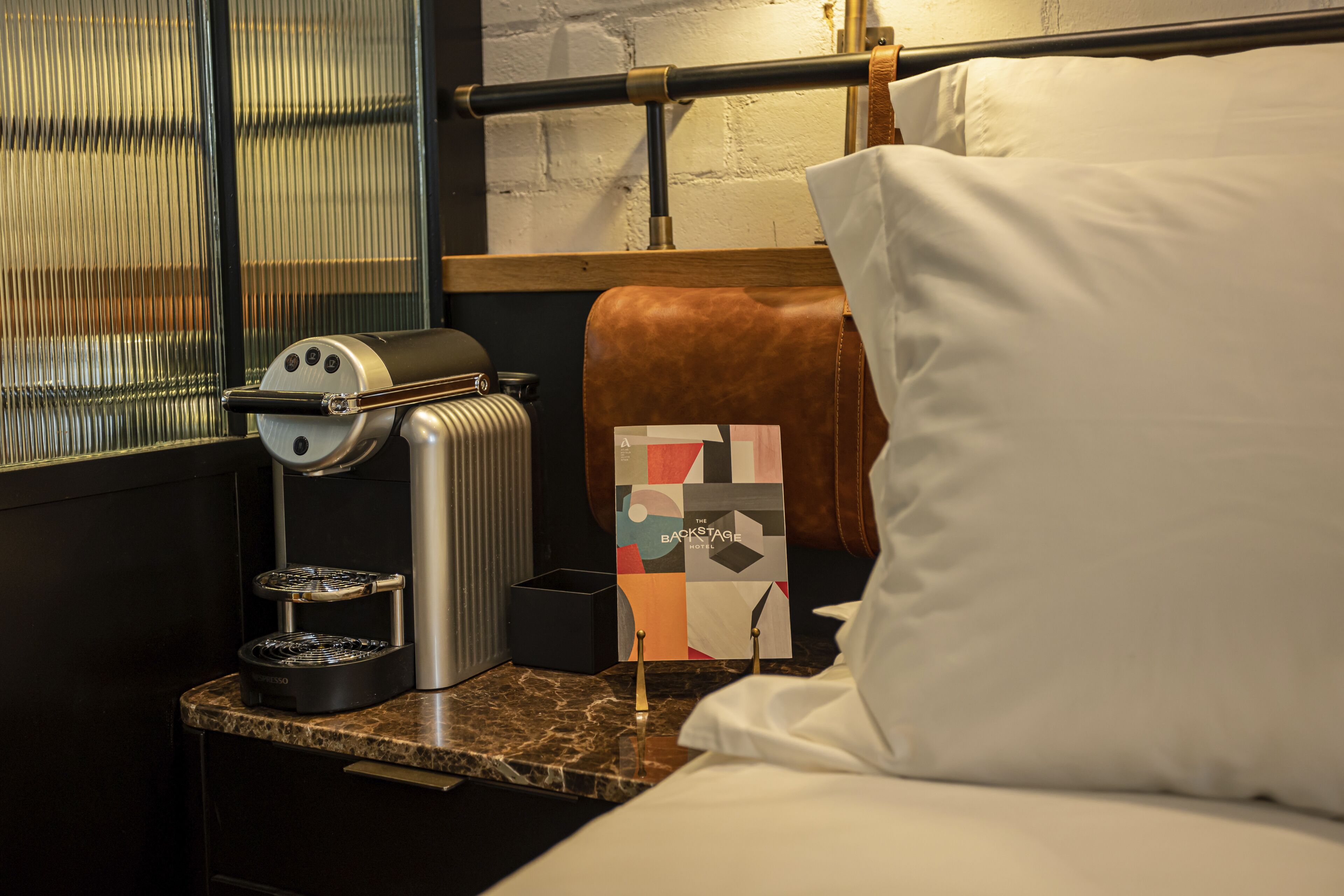 Habitación de hotel con cama, cafetera, almohada, manta y pared con diseño geométrico.