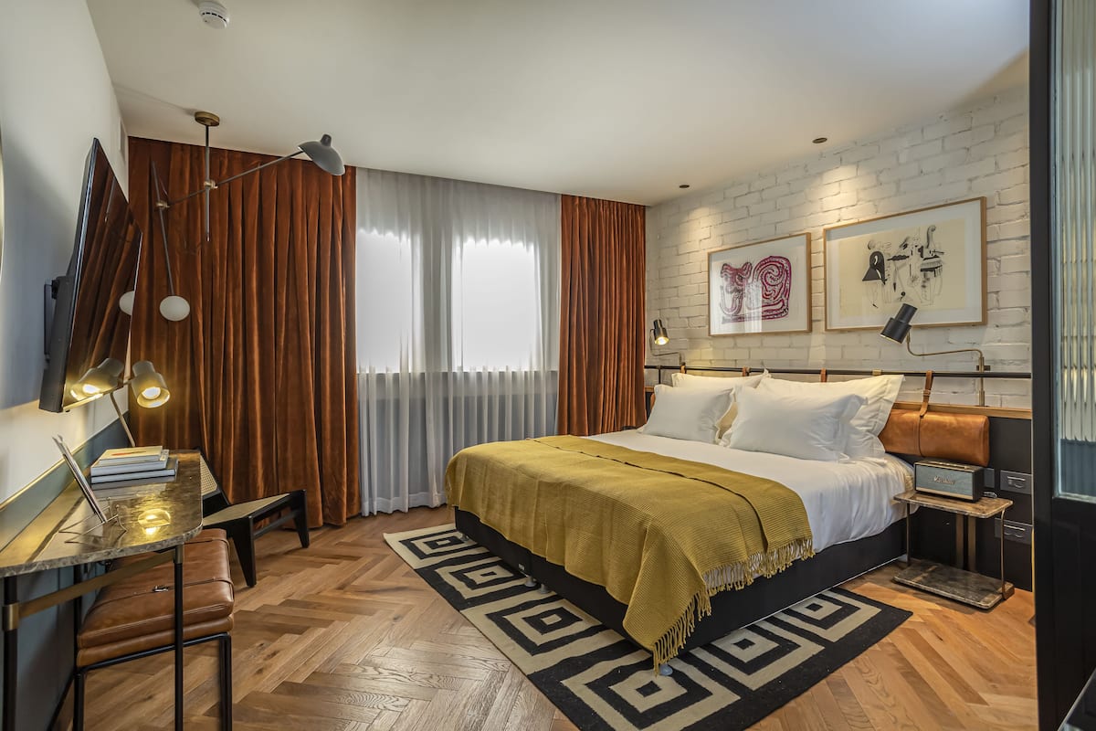 Een moderne slaapkamer met een groot bed, een bureau met een laptop, een staande lamp en een bakstenen muur met lijstwerken.