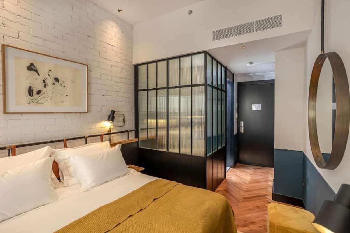 Een moderne hotelkamer met een bed, een groot raam, een spiegel en een kunstwerk in een lijst aan de muur.