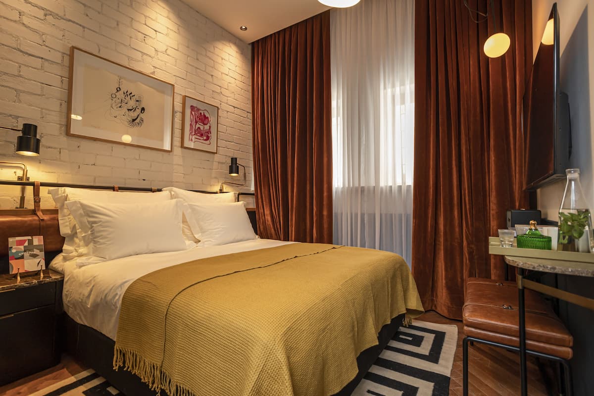 Een hotelkamer met een groot bed, een nachtkastje, een bureau met stoel en een raam met gordijnen.