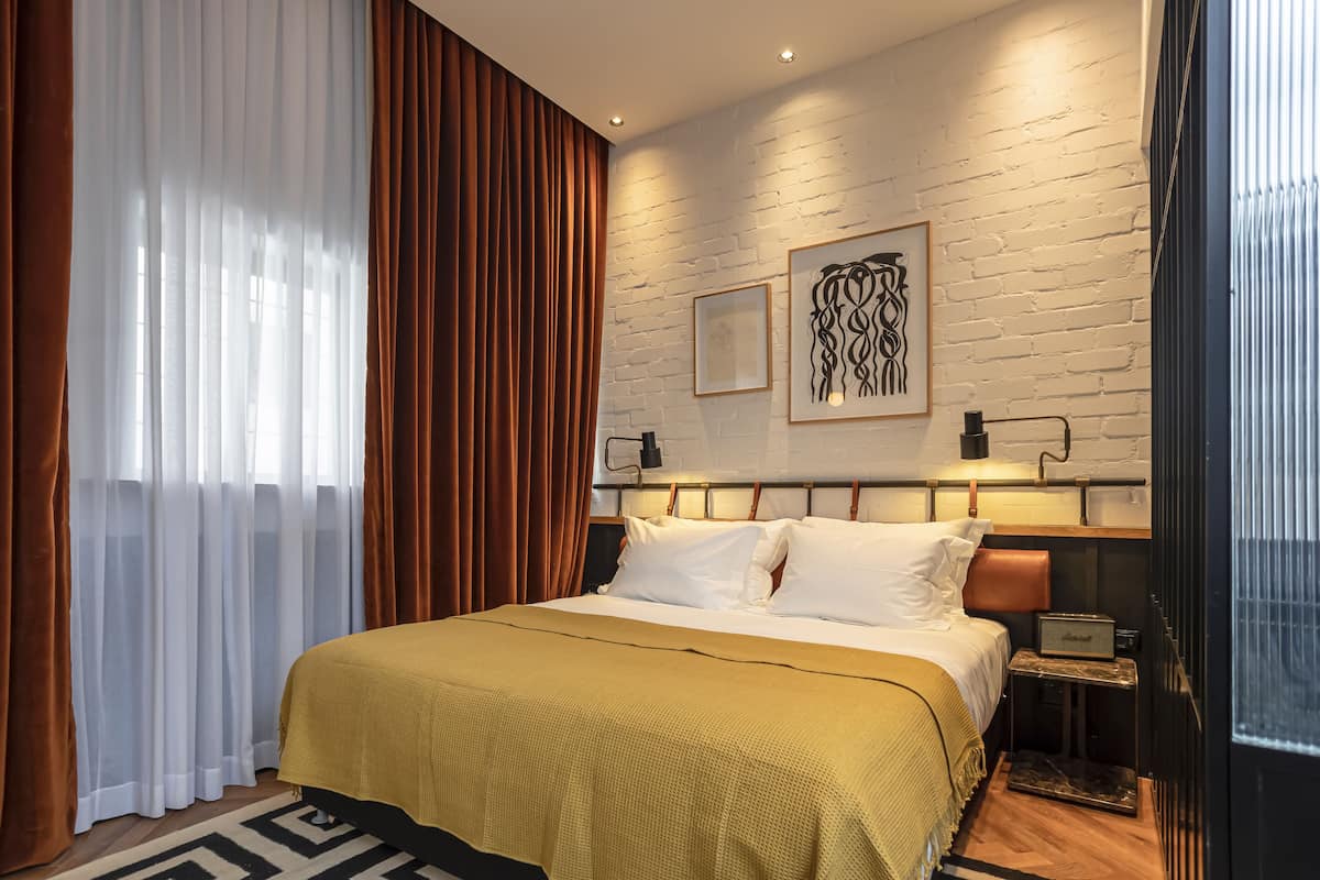 Een moderne hotelkamer met een groot bed, een nachtkastje met een lamp en een bakstenen muur met kunstwerk.