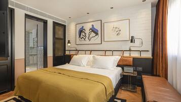 Une chambre d’hôtel moderne avec un grand lit, une table de chevet, un banc et des œuvres d’art accrochées au mur.