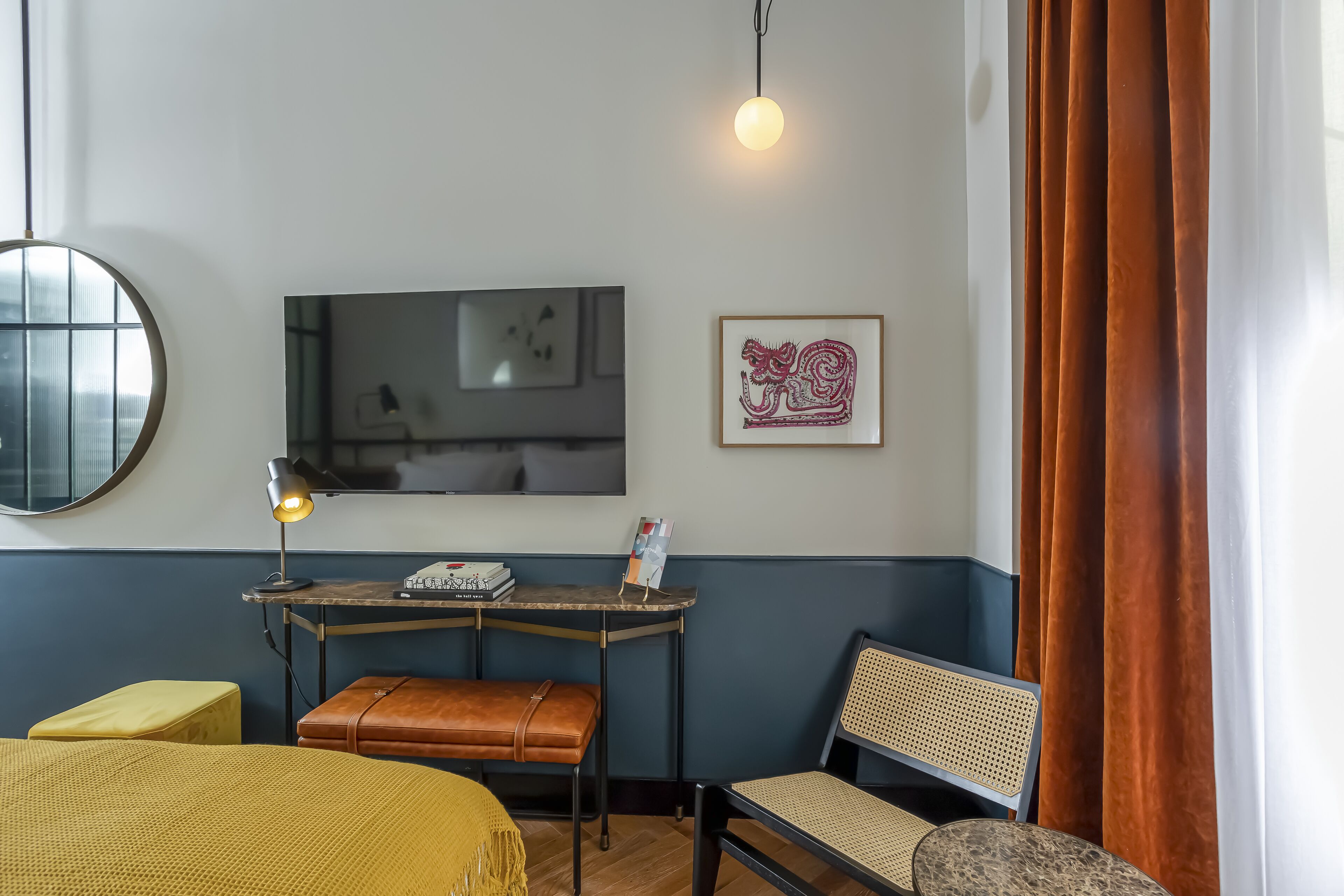 Habitación de hotel con cama, escritorio con lámpara, silla, televisor y un cuadro en la pared.
