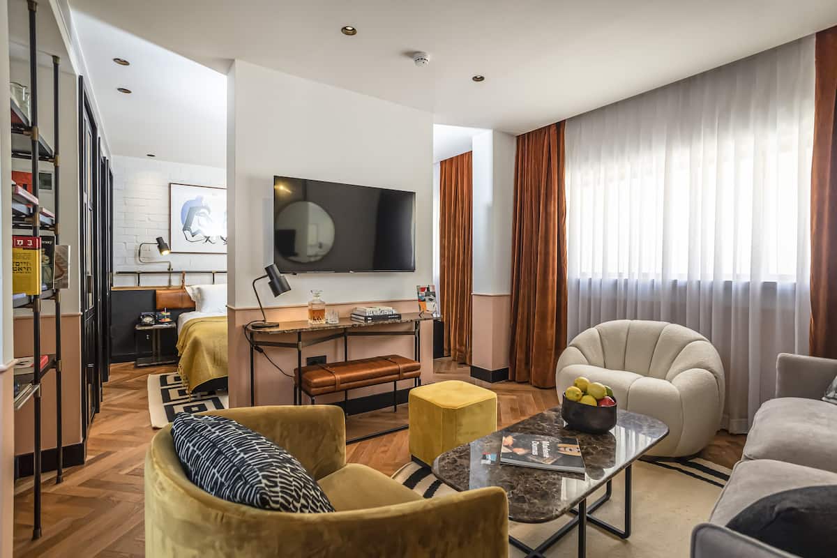 Een moderne woonkamer met een bank, fauteuil en poef, een flatscreen-televisie, en een eethoek met een tafel en bank.