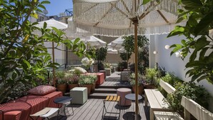 Um terraço no telhado com área de estar ao ar livre, plantas em vasos e um grande guarda-sol de fibra natural.
