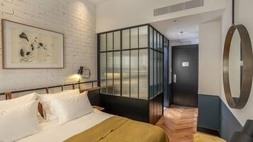 Habitación de hotel moderna con cama, un espejo grande, un cuadro abstracto enmarcado y un separador de vidrio original.