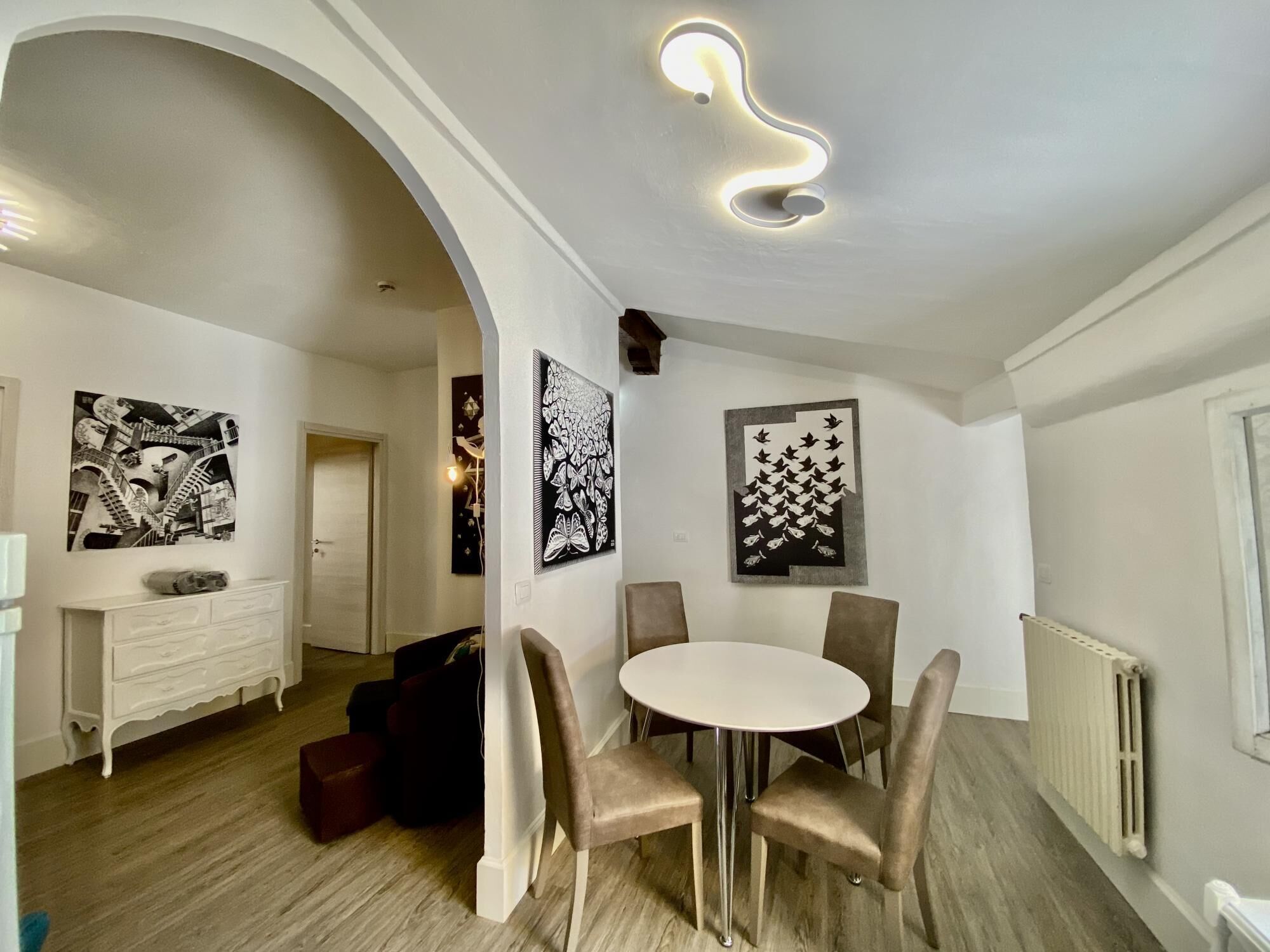 Un comedor con una mesa redonda y sillas, una chimenea blanca y obras de arte blanco y negro en las paredes.