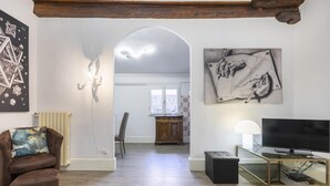 A living room with a brown sofa, a TV on a glass table, a painting on the wall, and a wooden ceiling. - Appartamento Ginori (Florence)