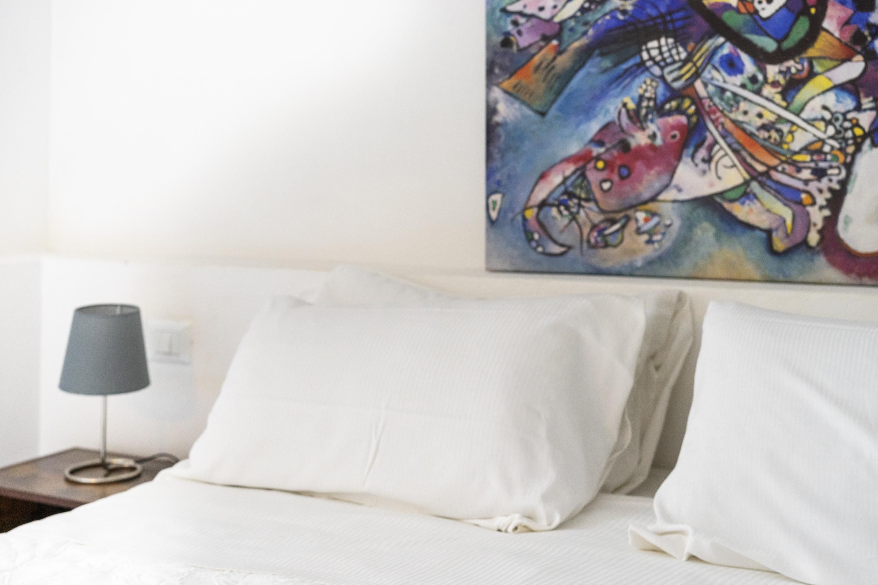 Una cama con sábanas blancas y un cuadro abstracto colorido encima.
