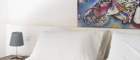 Una cama con sábanas blancas y un cuadro abstracto colorido encima.
