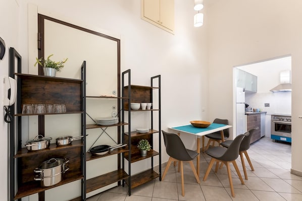 Cozinha compacta com área de refeições, com mesa e cadeiras, fogão e prateleiras com utensílios de cozinha.