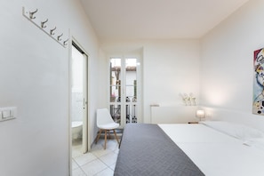 Quarto com cama, cadeira, porta para uma varanda e um quadro na parede.