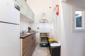A compact kitchen with a built-in oven, a stainless steel range hood, and a window with a view of the outside.
