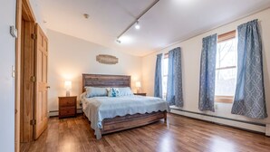 Een slaapkamer met een houten bed, twee nachtkastjes met lampen, een houten garderobe en een plafondlamp.