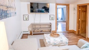 Een knusse woonkamer met een bank, een poef en een aan de muur bevestigde televisie.