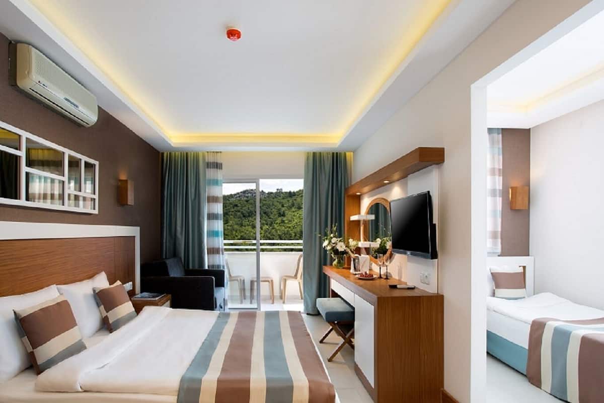 A hotel room with a large bed, a desk with a TV, a balcony with a view, and a ceiling with recessed lighting.
