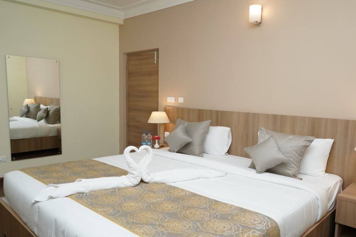 Quarto de hotel com uma cama grande, duas luminárias de cabeceira, um espelho e uma cabeceira de madeira.