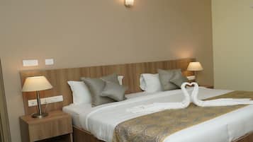 A hotel room with a wooden headboard, two bedside lamps, a bed with a white and gold patterned bedspread, and two towels arranged in a heart shape.